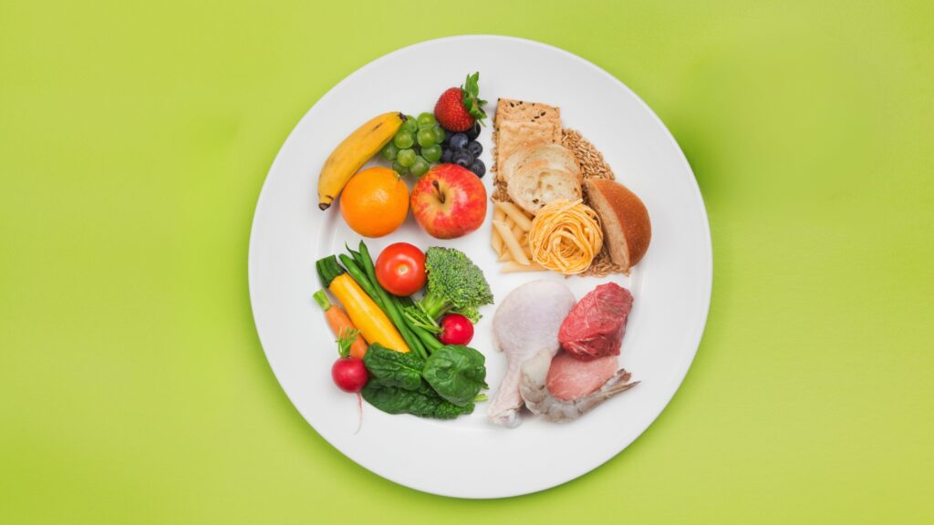 A balanced plate to stay healthy during holidays. Plate divided into three sections: half for fruits and vegetables, one quarter for lean protein sources, and the remaining quarter for whole grains or starchy vegetables.