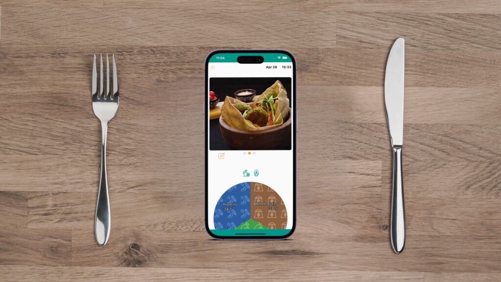 A smartphone displaying the JustaPlate food diary app interface, lying between a knife and a fork.