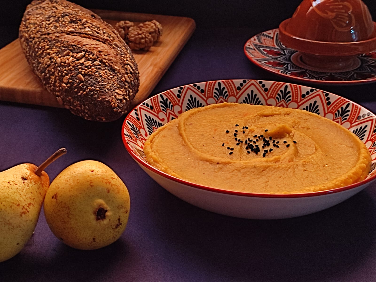 A bowl of red lentils sweet potato soup along side with bread and sone pears.