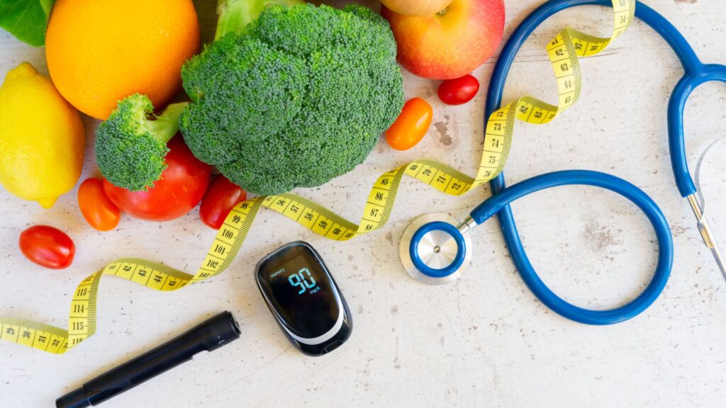 A stethoscope and diabetes kit rest beside a colorful array of fruits and vegetables